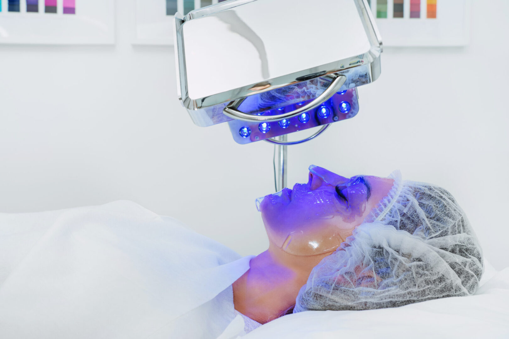 Young woman having blue LED light facial therapy treatment in beauty salon. Beautician wearing face mask maintaining safety procedures during appointment. Beauty, new normal and wellness LED Skin Care Spa