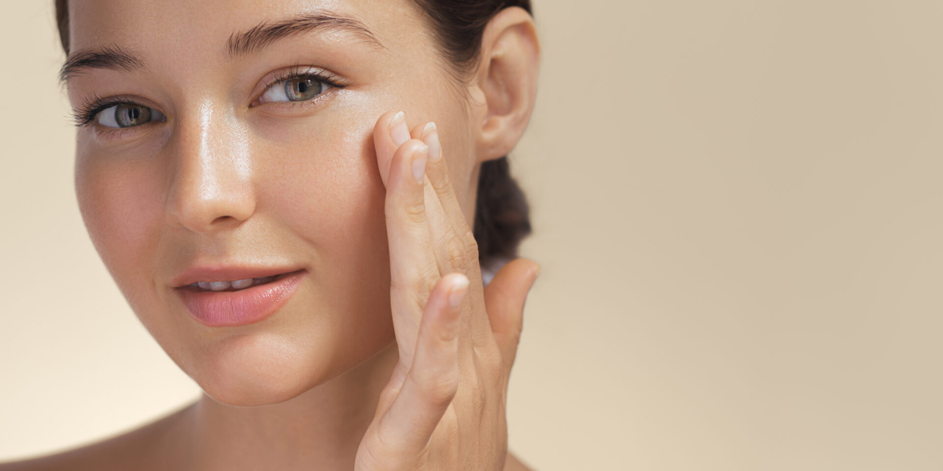 Skincare. Woman with beautiful face touching healthy facial skin portrait. Beautiful smiling Asian girl model with natural makeup enjoys glowing hydrated skin on beige background closeup. High-quality photo